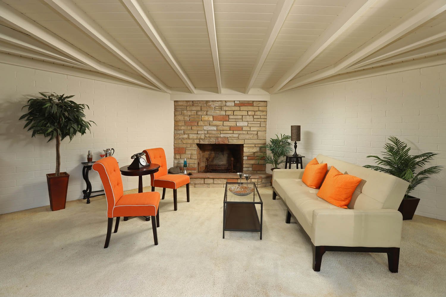 Staged den with orange accent chairs, cream sofa and brick fireplace